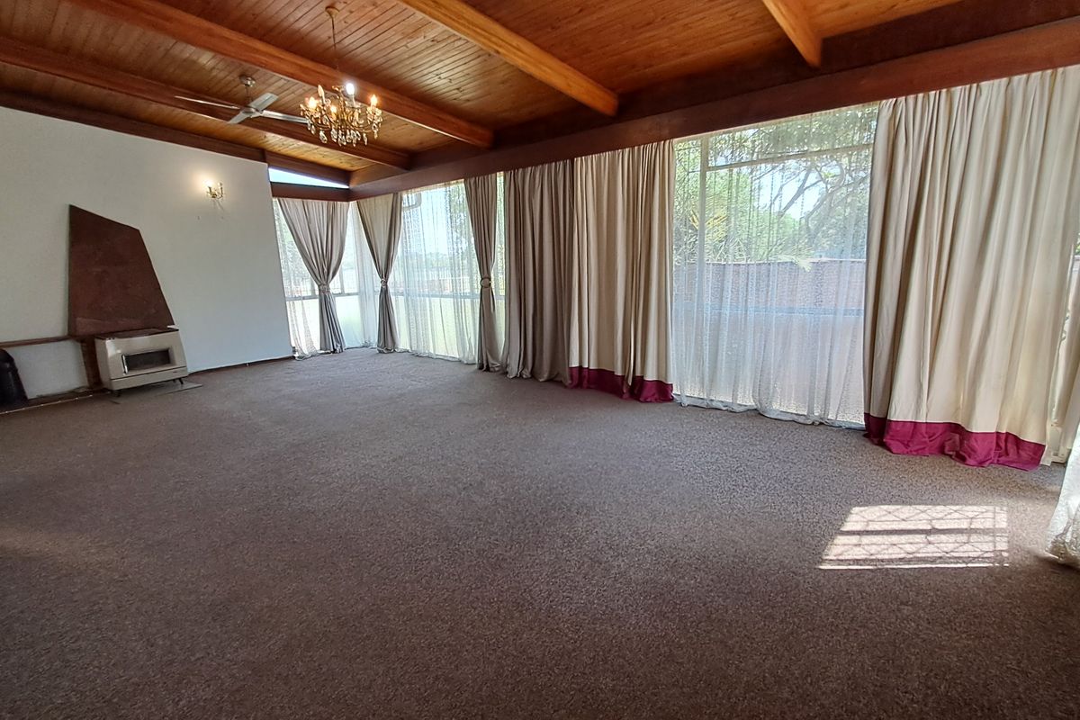 Spacious living room featuring a high exposed timber beam ceiling, a built-in wood-burning fireplace, and expansive windows providing ample natural light.
