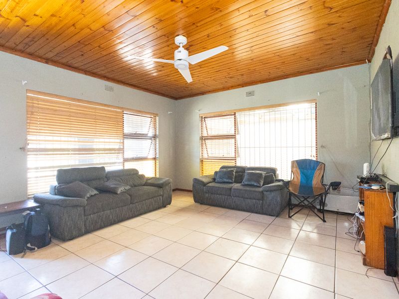 Spacious living room featuring a warm timber tongue and groove ceiling, ceramic tiled flooring, and large windows fitted with venetian blinds.