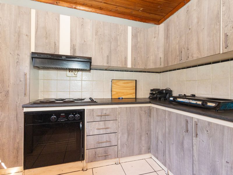 Functional kitchen featuring wood-look laminate cabinetry, built-in oven, electric hob, extractor fan, and tiled backsplash with a rustic timber ceiling.