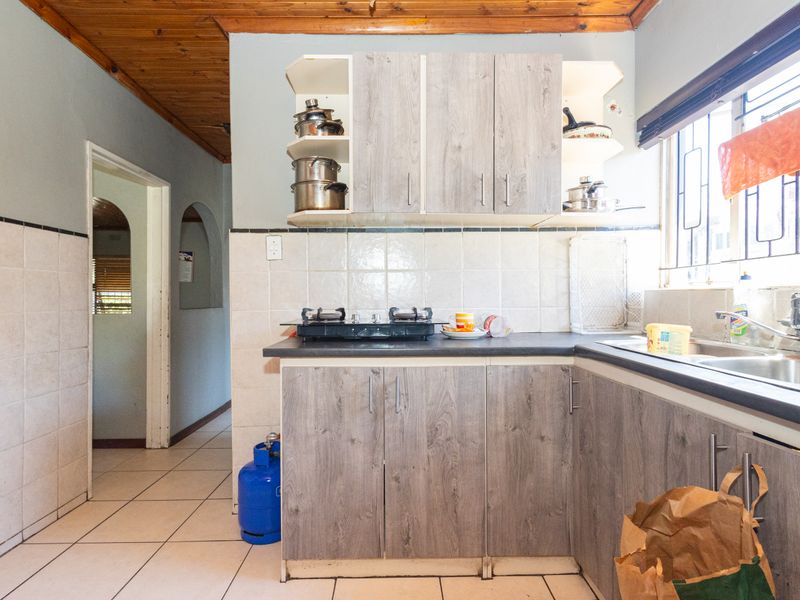 Functional kitchen featuring laminate cabinetry, tiled backsplash, double basin sink, and gas hob, with timber ceiling and tiled flooring throughout.