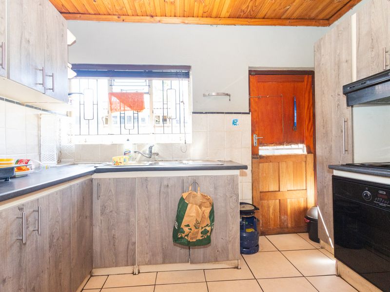 Functional kitchen featuring wood-look cabinetry, tiled flooring, a built-in oven with extractor fan, and direct access to an exterior door.