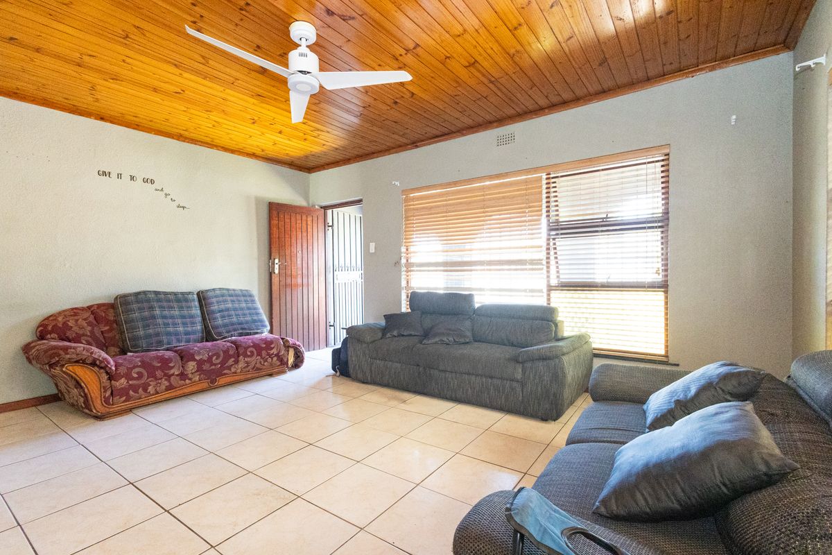 Spacious living room featuring a warm timber tongue and groove ceiling, ceiling fan, ceramic tiled flooring, and large windows with fitted venetian blinds.