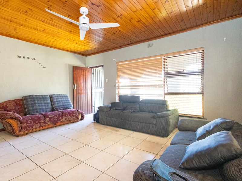 Spacious living room featuring a warm timber tongue and groove ceiling, ceiling fan, ceramic tiled flooring, and large windows with fitted venetian blinds.