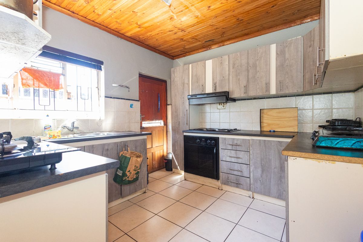 Functional kitchen featuring wood-look cabinetry, built-in oven and hob, tiled flooring, and a distinctive timber ceiling.