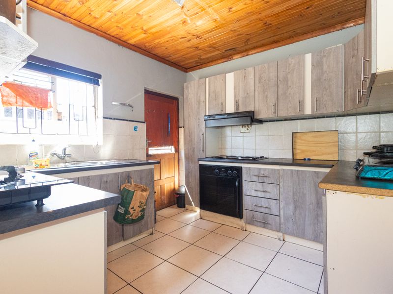 Functional kitchen featuring wood-look cabinetry, built-in oven and hob, tiled flooring, and a distinctive timber ceiling.