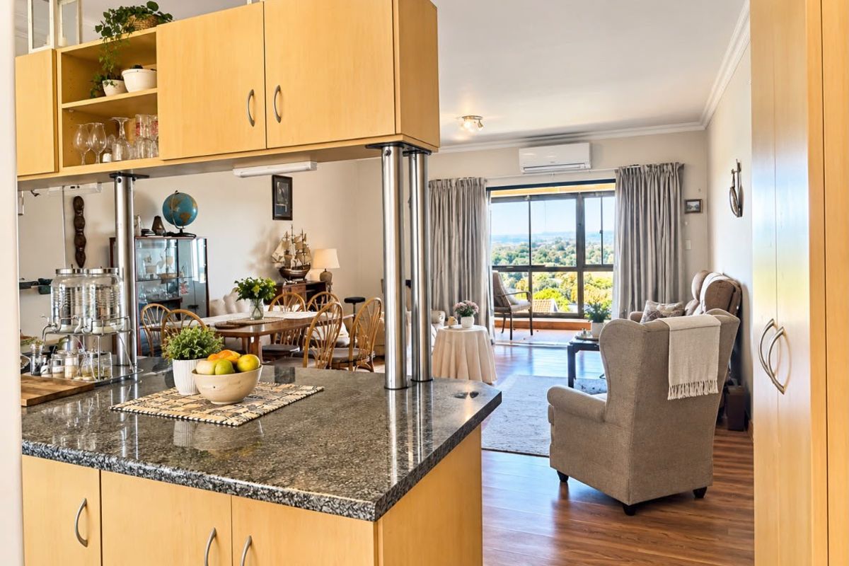 Open-plan living and kitchen area featuring granite countertops, light wood cabinetry, laminate flooring, and a sliding door leading to a balcony with scenic views.
