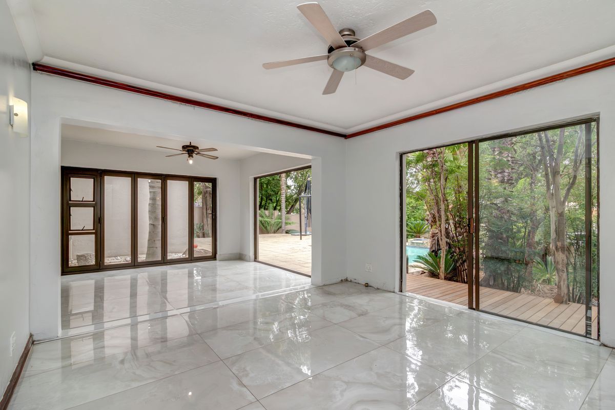 Spacious, light-filled living area featuring large sliding glass doors, polished tiled flooring, and ceiling fans, offering seamless access to the outdoor garden and pool area.