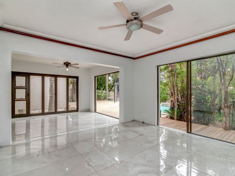 Spacious, light-filled living area featuring large sliding glass doors, polished tiled flooring, and ceiling fans, offering seamless access to the outdoor garden and pool area.