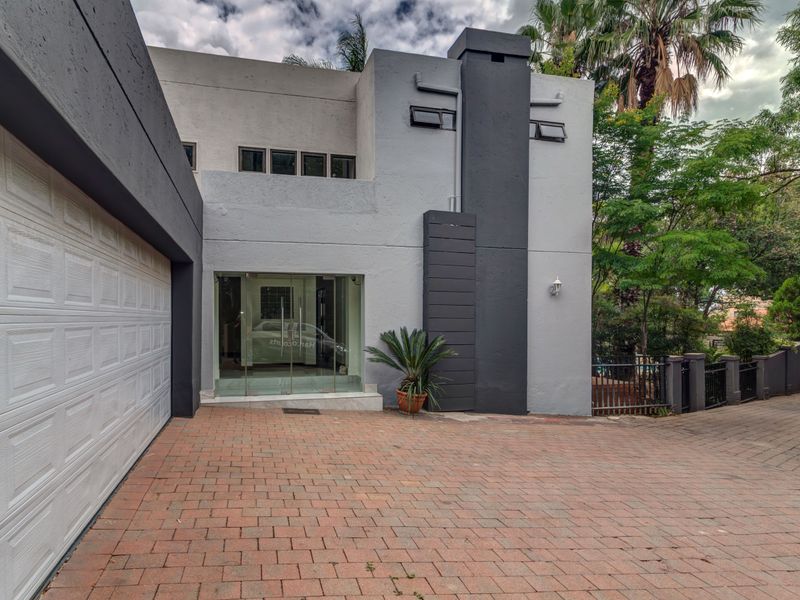Modern two-story residential facade featuring a paved driveway, double garage, and a prominent glass entrance door with contemporary grey and white exterior finishes.