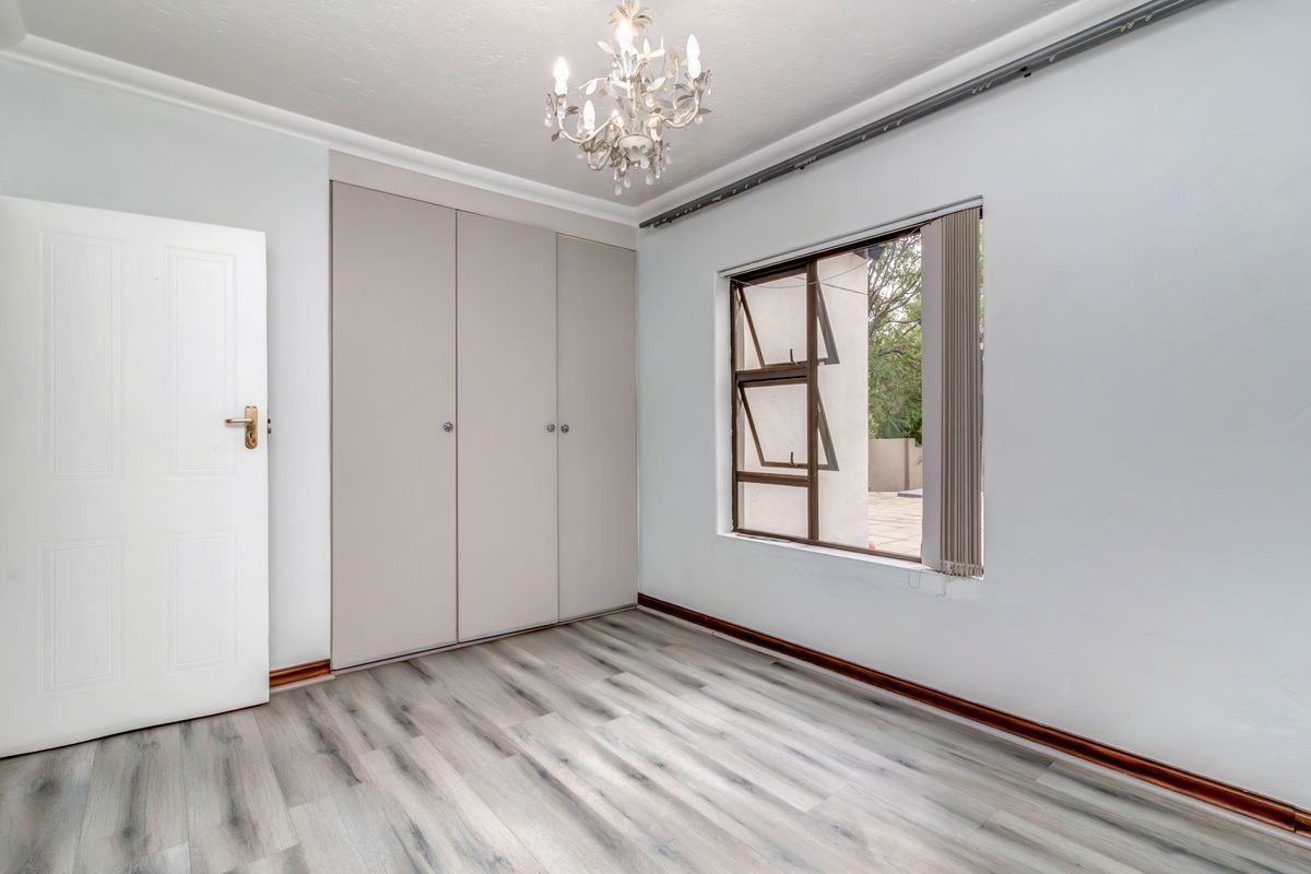 A bright, empty bedroom featuring modern laminate flooring, built-in cupboards, and a top-hung window, providing a clean and neutral space ready for personalization.