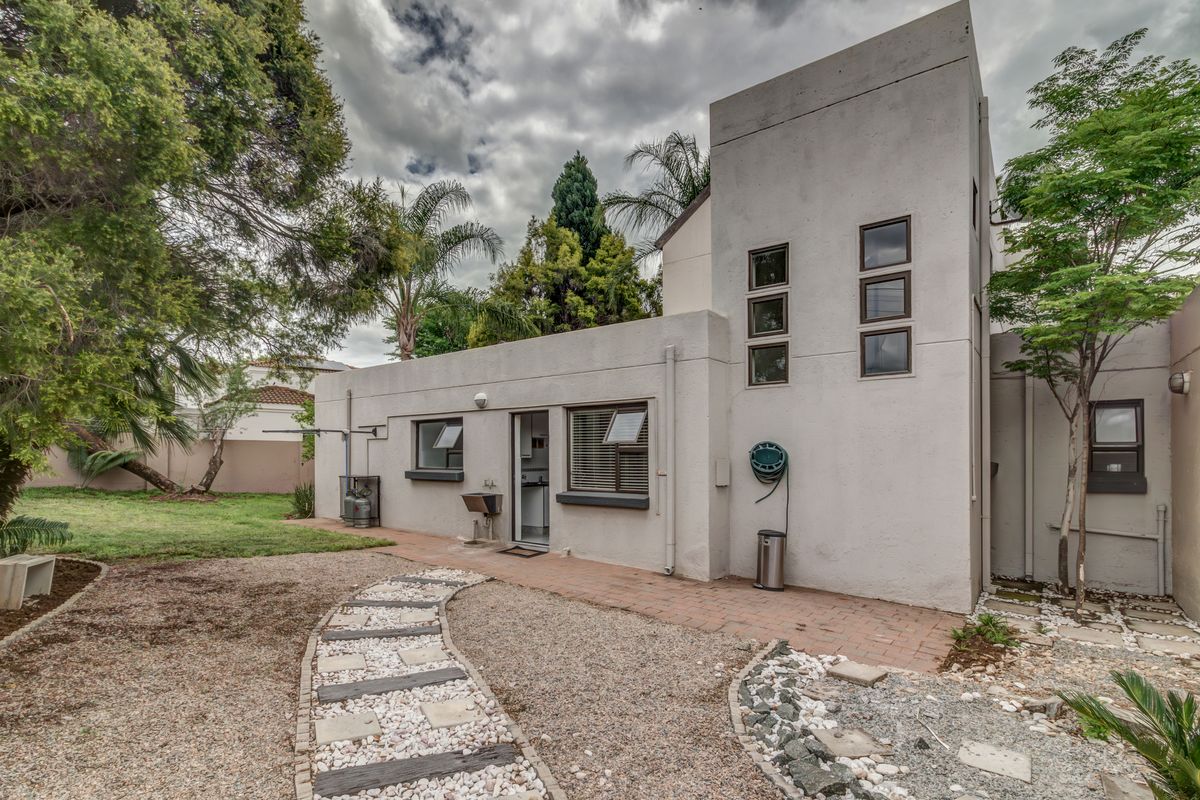 Rear exterior view of the property featuring a paved walkway, gravel garden area, and a functional external sink mounted to the stucco facade.