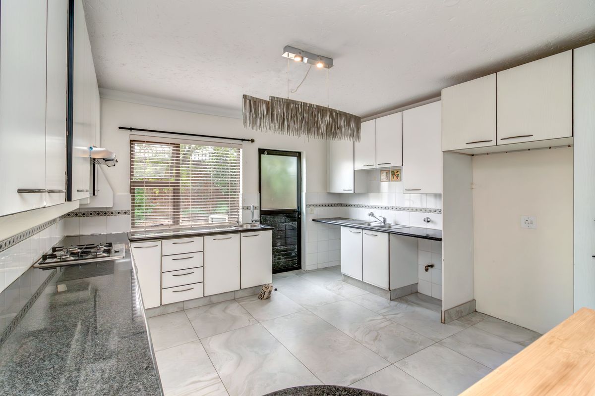 A functional kitchen featuring white cabinetry, granite countertops, a gas hob, and tiled flooring, offering a clean and practical workspace.