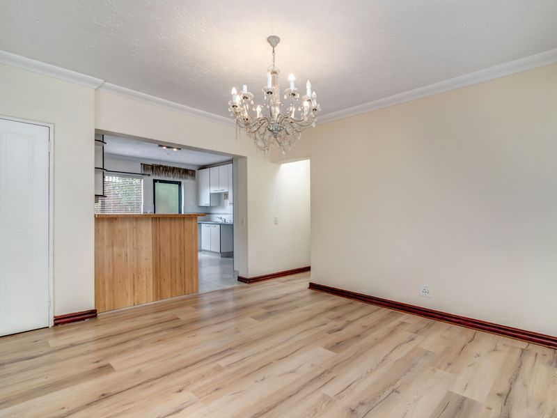 An open-plan living and dining area featuring light wood-look laminate flooring, a breakfast bar partition, and a decorative chandelier.