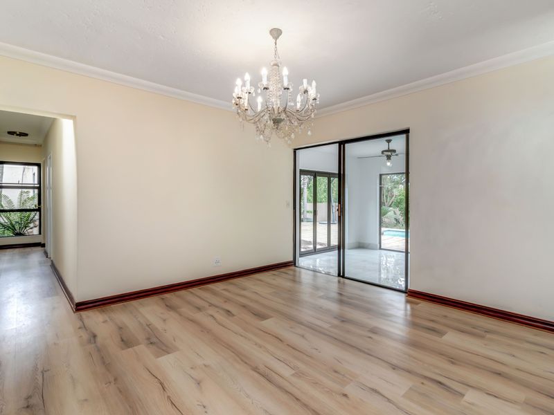 Spacious living area featuring light wood-look laminate flooring, elegant crystal chandelier, and sliding glass doors providing access to the outdoor patio and pool area.