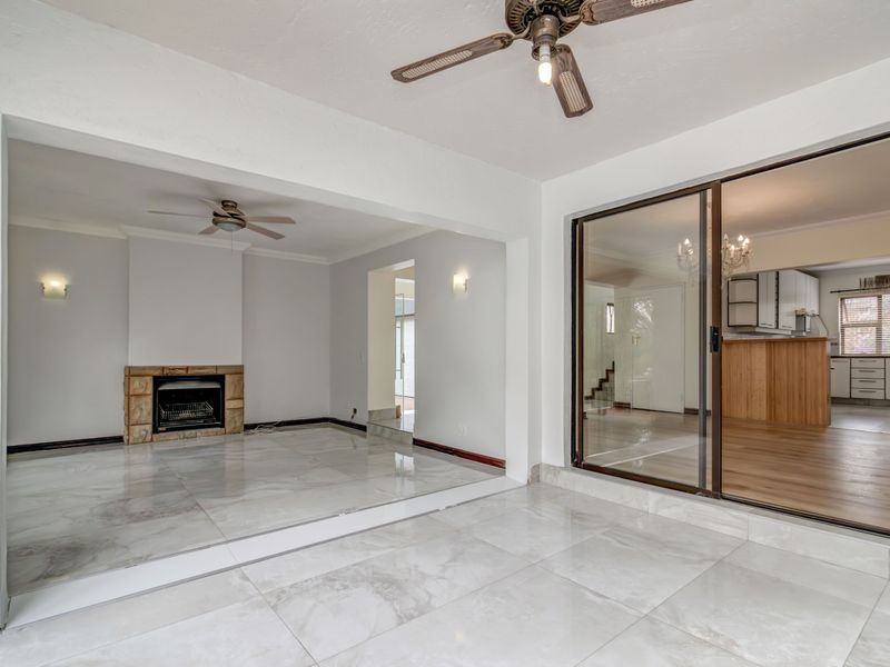 Spacious open-plan living area featuring polished marble-look tiles, a stone fireplace, and large sliding glass doors leading to an adjacent room.