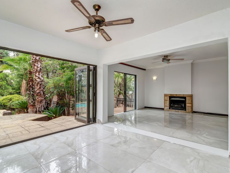 Spacious open-plan living area featuring large bi-fold doors opening to the garden, a stone fireplace, and polished tiled flooring throughout.