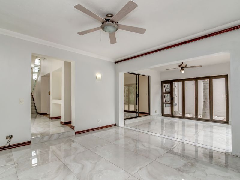 Spacious, light-filled living area featuring polished marble-look tiled flooring, ceiling fans, and large sliding glass doors leading to an outdoor space.
