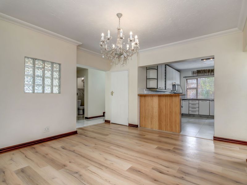 Open plan living area featuring timber laminate flooring, a breakfast bar, and a view into the adjacent kitchen and hallway.