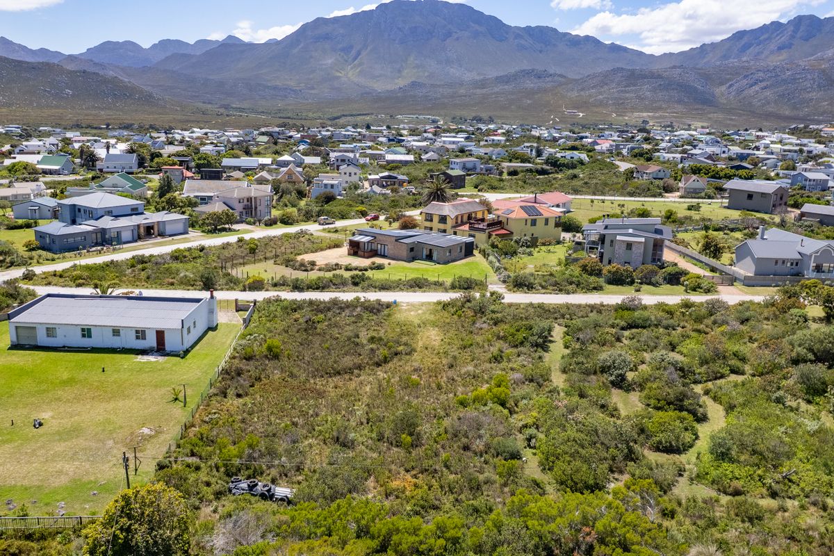 An aerial view of a vacant residential plot situated in a coastal neighborhood with mountain views.
