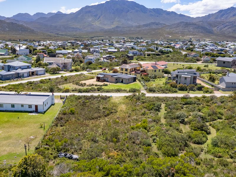 An aerial view of a vacant residential plot situated in a coastal neighborhood with mountain views.