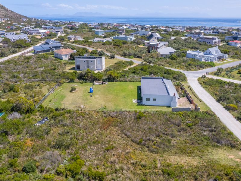 Aerial view of a vacant residential plot featuring established lawn, perimeter fencing, and convenient access to local gravel roads in a coastal setting.