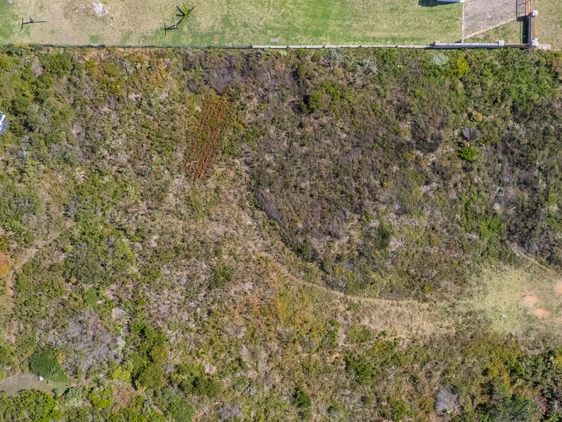 An aerial view of a vacant residential plot featuring natural vegetation and direct access to an adjacent gravel road.