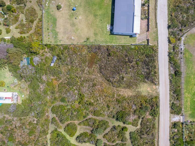 An aerial view of a vacant residential plot featuring natural vegetation and direct access to an unpaved road.