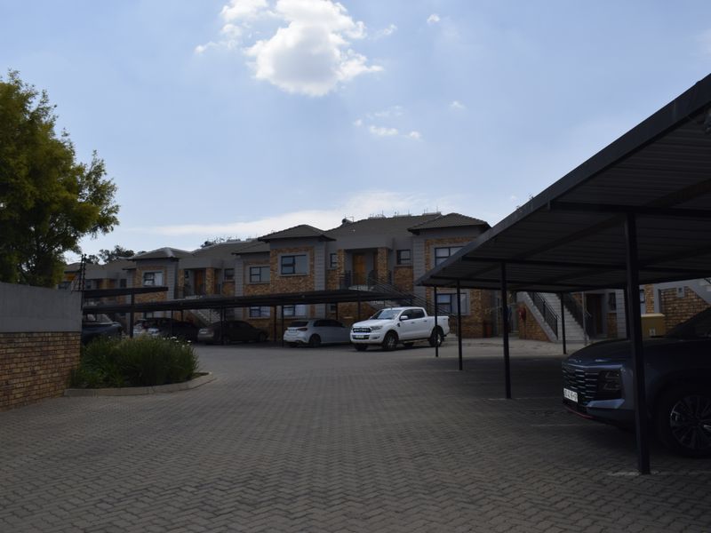 Front exterior view of a townhouse complex featuring brick facades, tiled roofing, and covered carport parking spaces.