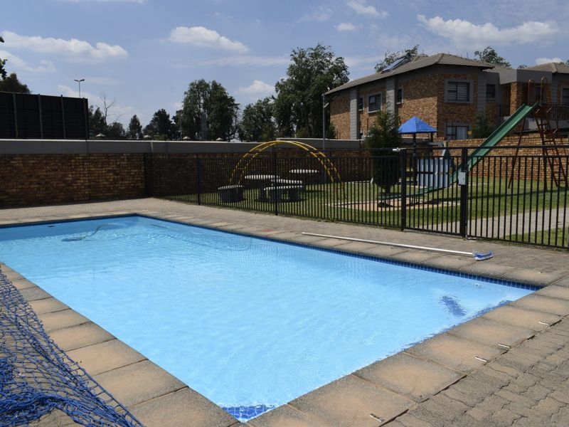 Communal swimming pool area featuring paved surround, metal fencing, and an adjacent playground facility within the townhouse complex.