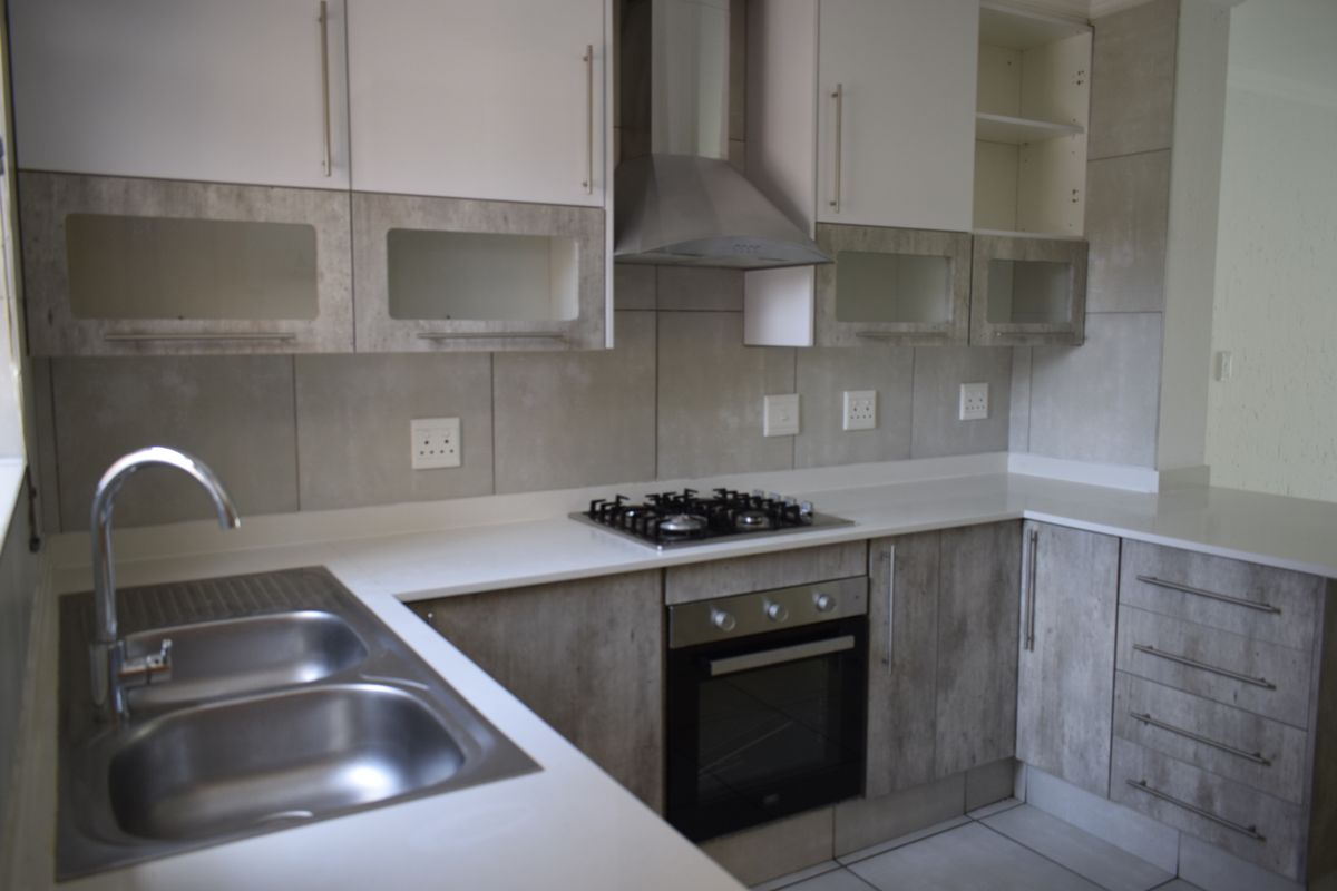 Modern kitchen featuring stone countertops, built-in cabinetry, stainless steel sink, gas hob, and integrated oven with extractor fan.