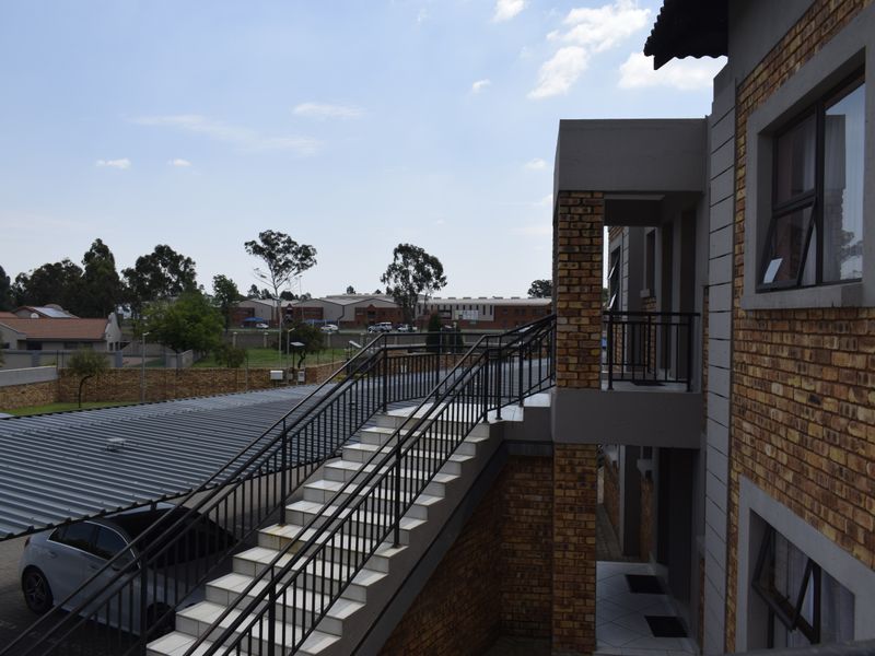 Exterior view of a townhouse complex featuring a brick facade, external staircase with metal railings, and a covered carport area.