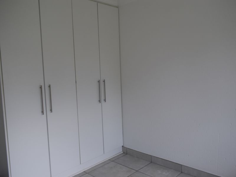 A clean, empty bedroom space featuring modern white built-in cupboards and neutral tiled flooring, ready for personalization.