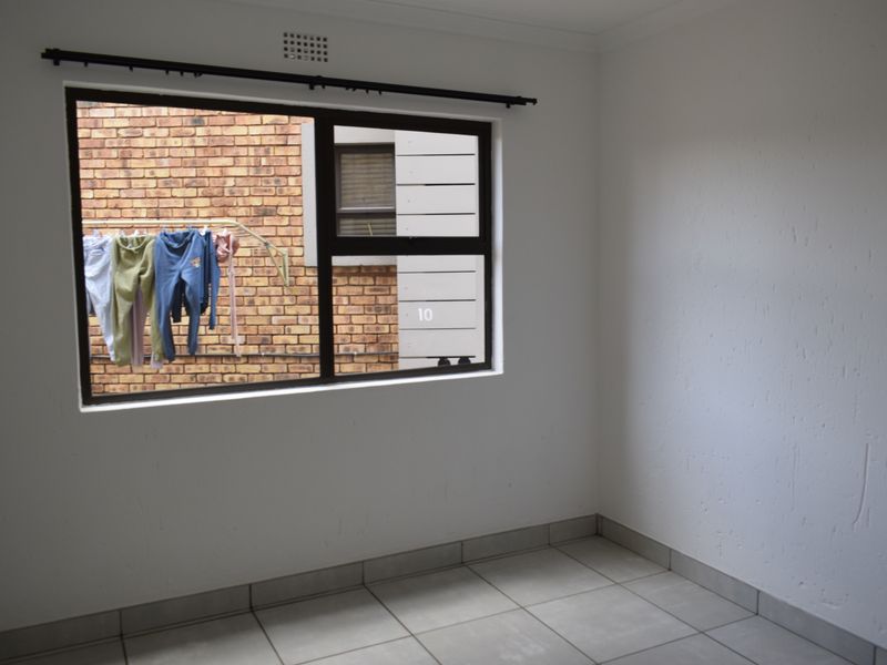 A vacant bedroom featuring neutral tiled flooring and an aluminium window frame, offering a blank canvas for personalization.