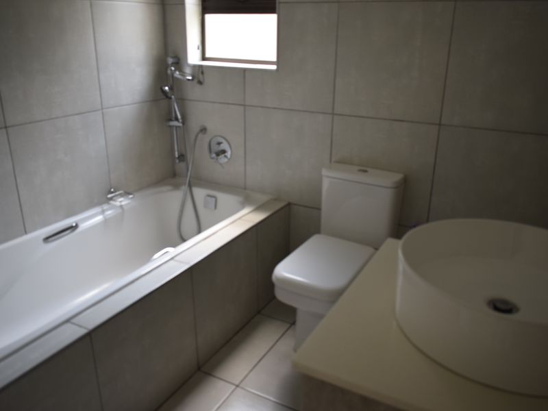 A clean, modern bathroom featuring a built-in bathtub with shower mixer, a white toilet, and a contemporary vessel sink on a vanity countertop.