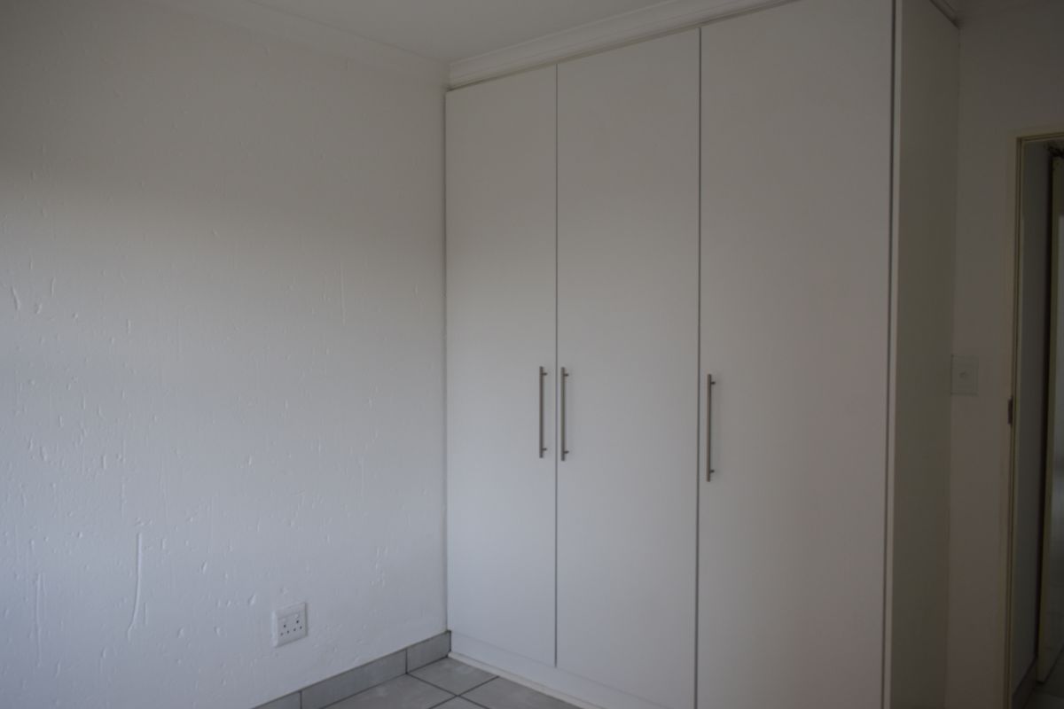 A clean, empty bedroom featuring neutral tiled flooring and modern white built-in cupboards, providing ample storage space.