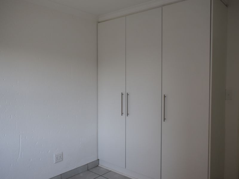 A clean, empty bedroom featuring neutral tiled flooring and modern white built-in cupboards, providing ample storage space.