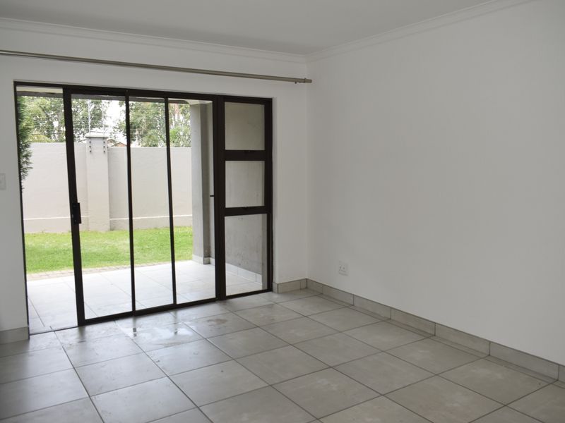 An empty living room featuring neutral tiled flooring and a large sliding glass door providing direct access to the rear patio and garden.
