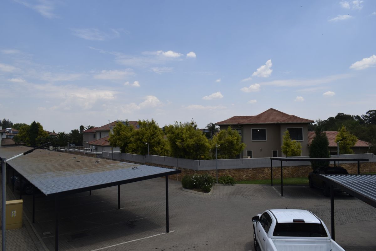An elevated view of a townhouse complex parking area featuring paved driveways, covered carports, and surrounding perimeter walls.