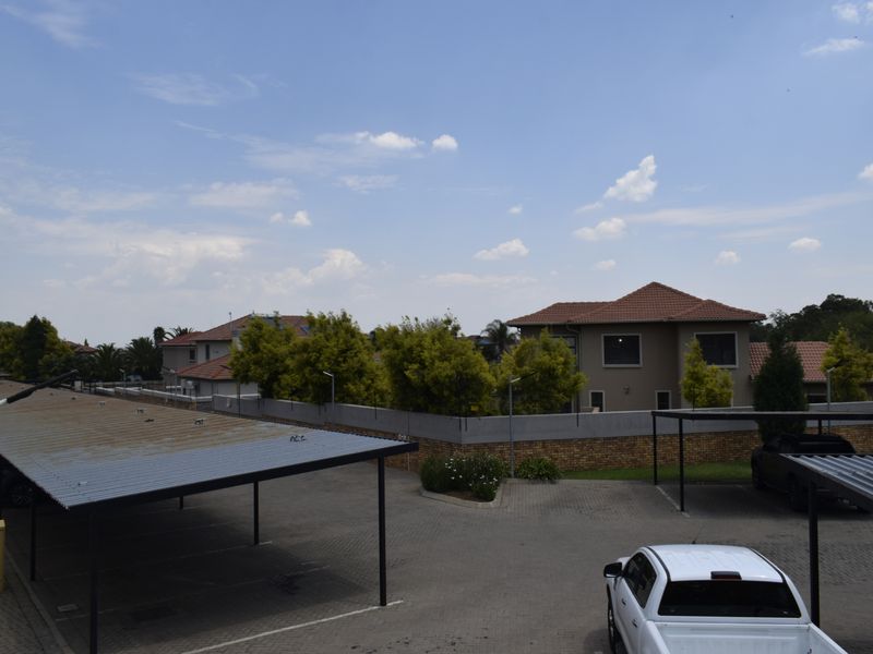 An elevated view of a townhouse complex parking area featuring paved driveways, covered carports, and surrounding perimeter walls.