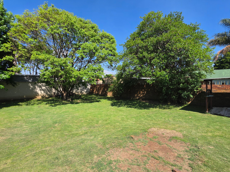 A spacious private garden featuring a well-established lawn, mature trees, and secure perimeter brick walling.