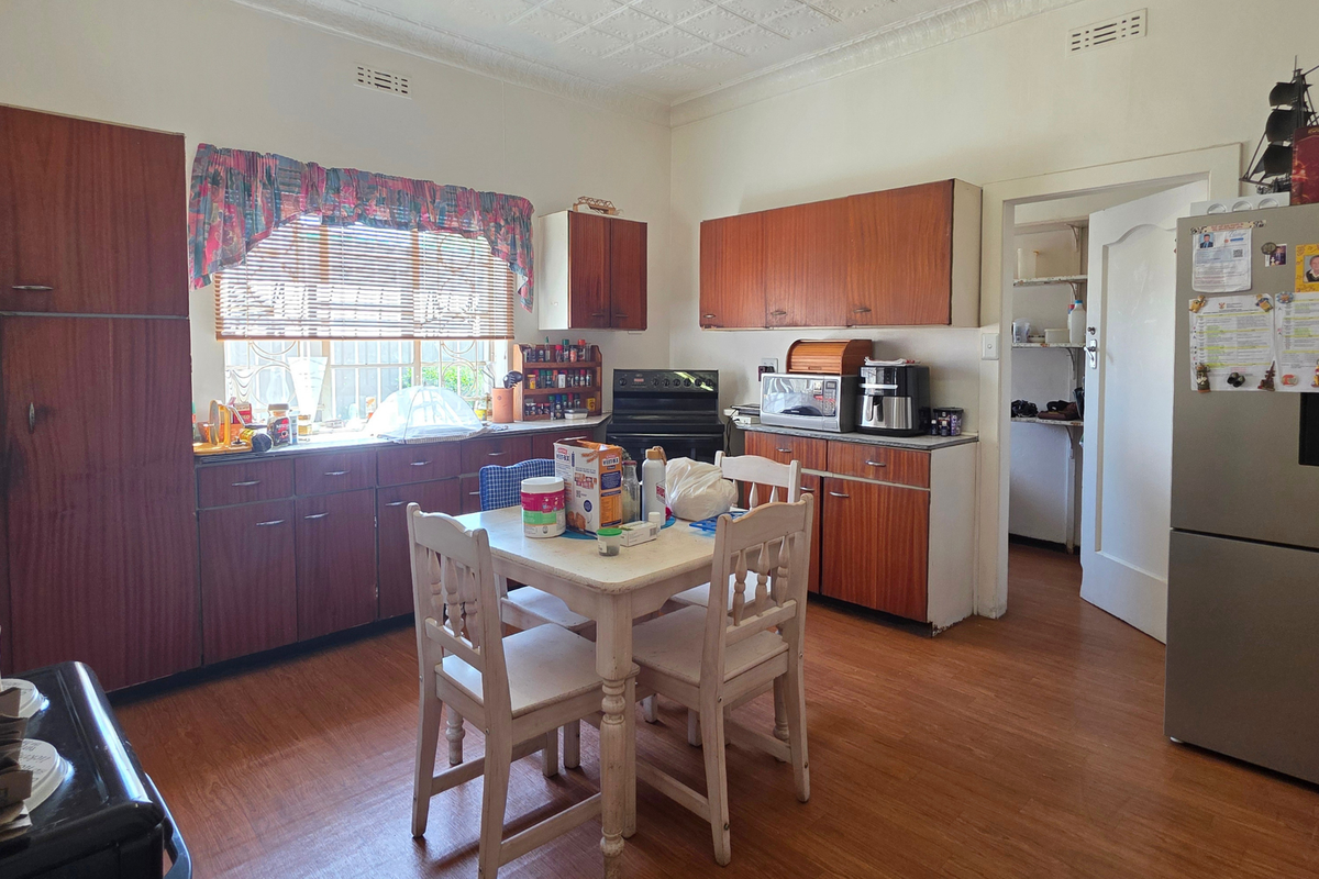 A dated kitchen featuring original wooden cabinetry, laminate flooring, and a separate scullery area, offering significant potential for a modern renovation.