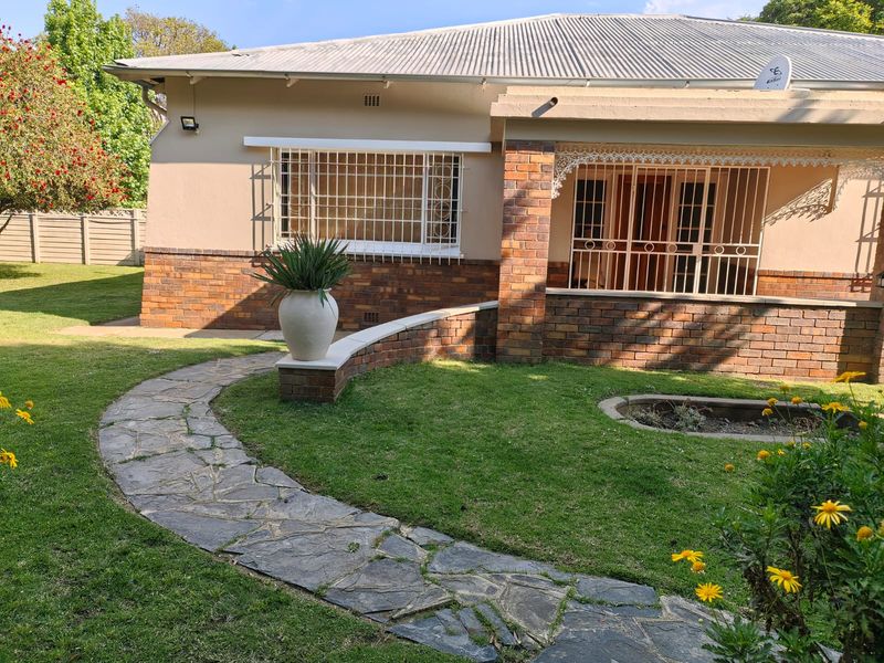 Front elevation of a brick house featuring a stone paved walkway, manicured lawn, and security bars on windows and entrance.
