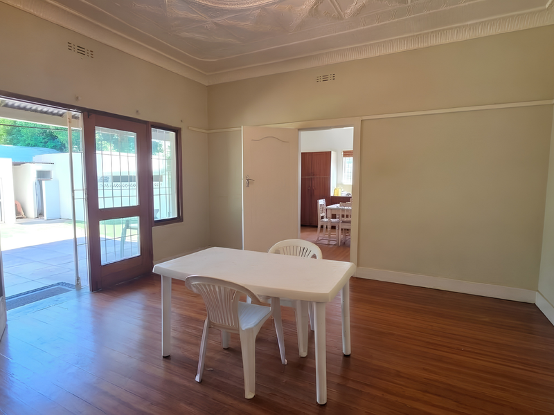 Spacious living area featuring polished hardwood floors, ornate ceiling detailing, and direct access to an outdoor patio through timber-framed glass doors.