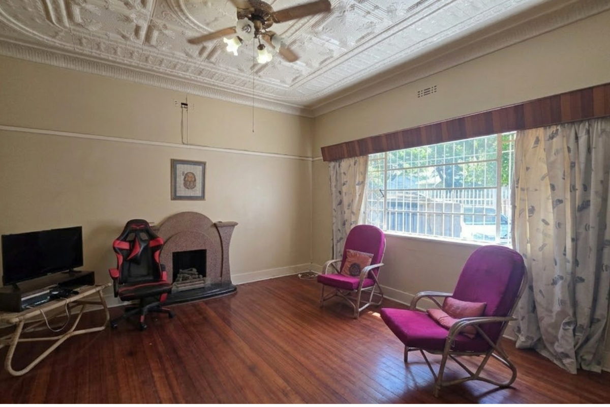 Spacious living room featuring original pressed metal ceilings, hardwood flooring, and a character fireplace, offering a classic foundation for modern updates.
