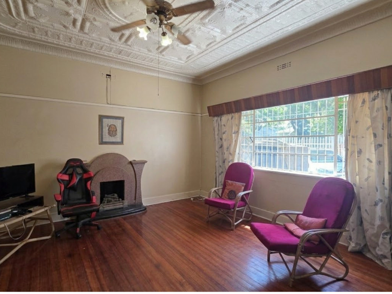 Spacious living room featuring original pressed metal ceilings, hardwood flooring, and a character fireplace, offering a classic foundation for modern updates.