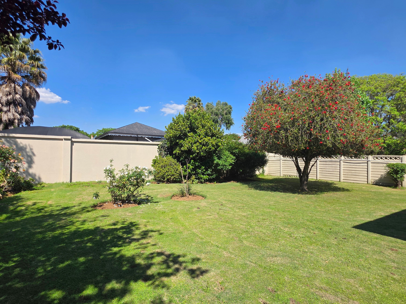 A well-maintained private garden featuring a lush green lawn, mature trees, and secure perimeter wall and fencing.