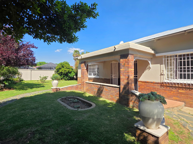 A well-maintained front exterior featuring classic brickwork, a covered porch with decorative fretwork, security bars on windows, and a landscaped garden with stone pathways.