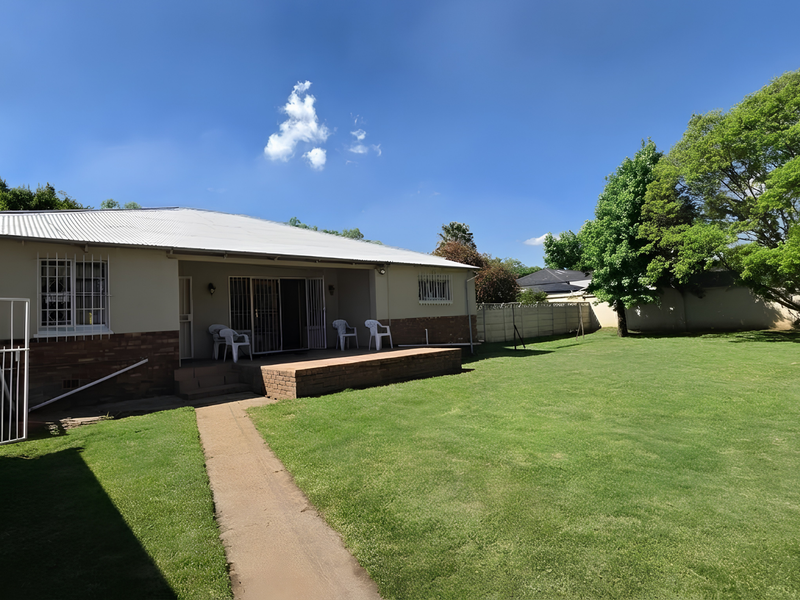 Rear view of the house featuring a corrugated metal roof, brick patio, sliding glass doors, and a spacious garden with a concrete boundary wall.