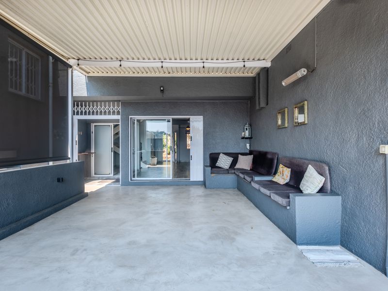 A covered patio area featuring a built-in concrete bench, corrugated metal roofing, and sliding glass door access to the interior living space.