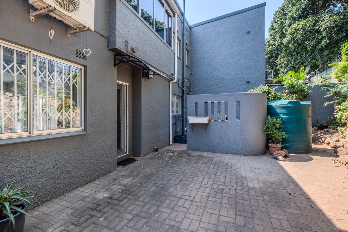 Rear exterior view of the townhouse featuring a paved courtyard, masonry privacy wall, and a water storage tank.